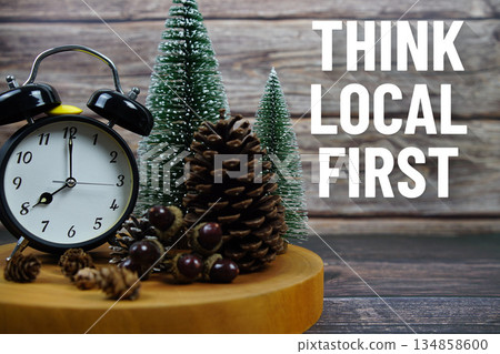 Festive holiday scene featuring a vintage alarm clock, pinecones, and miniature Christmas trees on a wooden base, with the text "Think Local First" encouraging support for local businesses during Festive holiday scene featuring a vintage alarm clock, pinecones, and miniature Christmas trees on a wooden base, with the text "Think Local First" encouraging support for local businesses during 134858600