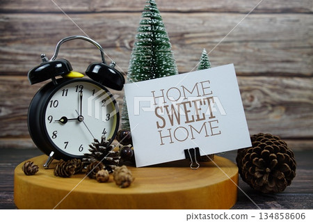 Festive holiday scene featuring a vintage alarm clock, pinecones, and miniature Christmas trees on a wooden base, with the text "Home Sweet Home" encouraging support for local businesses during the ho 134858606