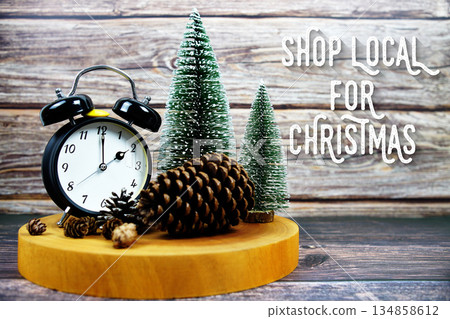 Festive holiday with Alarm clock, pinecones, and miniature Christmas trees on a wooden base with the text "Shop Local for Christmas" encouraging support for local businesses during the holiday season Festive holiday with Alarm clock, pinecones, and miniature Christmas trees on a wooden base with the text "Shop Local for Christmas" encouraging support for local businesses during the holiday season 134858612
