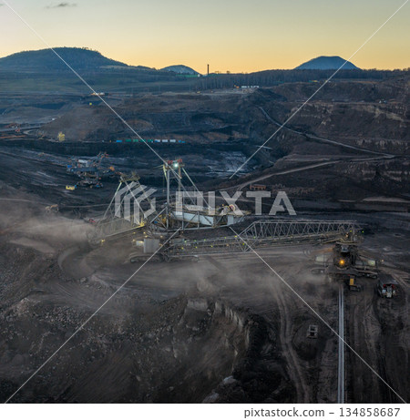 Aerial view of an active coal mining site showcases heavy machinery and smoke billowing into the air 134858687