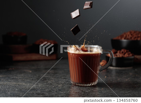 Pieces of dark chocolate fall into a mug of cocoa drink. 134858760