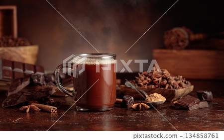 Glass mug of hot chocolate with ingredients on a brown background. 134858761