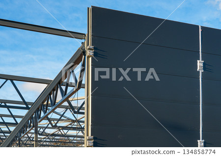Steel frame structure with sandwich wall panels on modern industrial warehouse under construction Steel frame structure with sandwich wall panels on modern industrial warehouse under construction 134858774