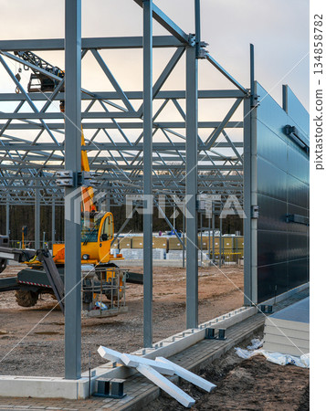 Steel frame construction site with workers assembling sandwich wall panels for industrial building 134858782
