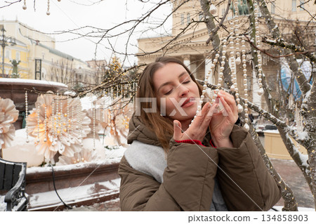 Woman touches hanging pearl garlands near a snow-covered fountain and large flower installation in front of the Bolshoi Theatre 134858903