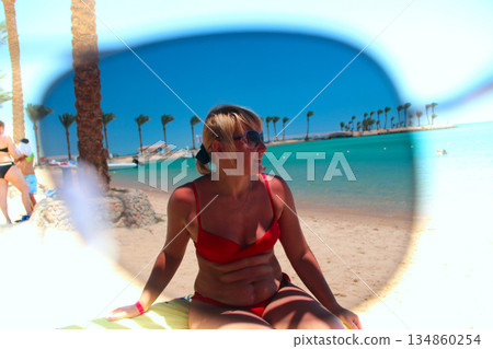 Looking through sunglasses at beach with woman sea and palm trees Looking through sunglasses at beach with woman sea and palm trees 134860254
