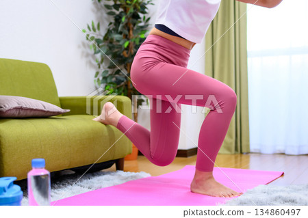 Bulgarian squat - Young woman wearing yoga wear training her lower body indoors - Butt lifting - Trimming Bulgarian squat - Young woman wearing yoga wear training her lower body indoors - Butt lifting - Trimming 134860497