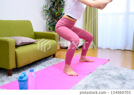 Squats Young woman wearing yoga wear training her lower body indoors Hip up Squats Young woman wearing yoga wear training her lower body indoors Hip up 134860703