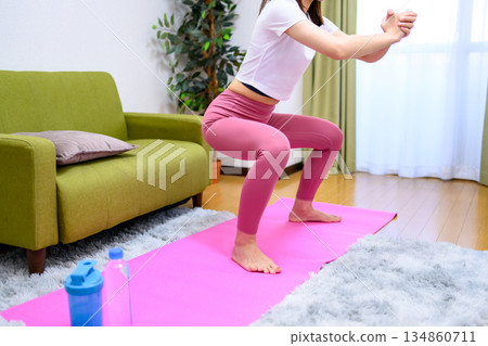 一位身穿瑜珈服的年輕女子在室內進行下肢深蹲訓練，並抬起臀部。 134860711