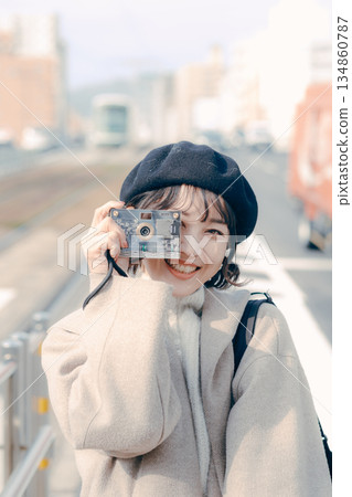 一位三十多歲的女性面帶微笑，手持相機，拍攝了一張肖像照。 134860787