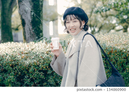 A woman in her 30s walking with a smile and holding a coffee cup at a tourist spot A woman in her 30s walking with a smile and holding a coffee cup at a tourist spot 134860900