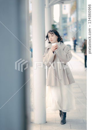 Portrait of a woman in her 30s waiting at a bus stop while drinking coffee 134860966