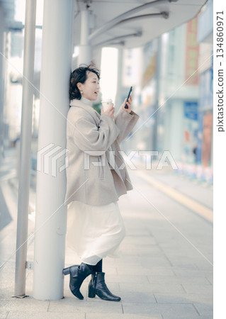 Portrait of a woman in her 30s waiting at a bus stop while drinking coffee 134860971