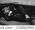 A vintage portrait of a six-year-old boy lying on a sofa reading a book. Retro photo from 1973. 134860988
