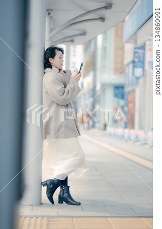 一位三十多歲的女子在公車站等車時正在使用智慧型手機 134860991