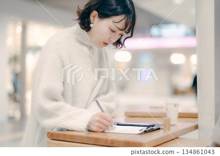 一位三十多歲的女子在街上邊工作邊寫筆記 一位三十多歲的女子在街上邊工作邊寫筆記 134861043