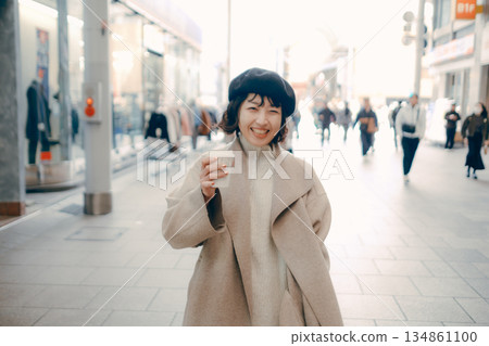 一位女士手捧一杯咖啡走在城市裡。 一位女士手捧一杯咖啡走在城市裡。 134861100