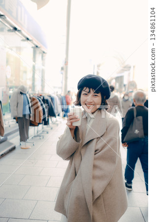A woman walking in the city with a cup of coffee A woman walking in the city with a cup of coffee 134861104