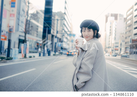 A woman walking in the city with a cup of coffee 134861110