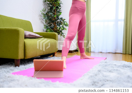 一位身穿瑜珈服的年輕女子雙腿張開，準備做深蹲，在室內進行下肢訓練，並抬起臀部。 134861153