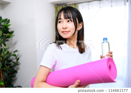 日本女子身穿瑜珈服和緊身褲,在房間裡鋪好瑜珈墊,準備了水,開始運動。 日本女子身穿瑜珈服和緊身褲,在房間裡鋪好瑜珈墊,準備了水,開始運動。 134861577