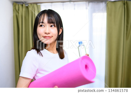 日本女子身穿瑜珈服和緊身褲,在房間裡鋪好瑜珈墊,準備了水,開始運動。 日本女子身穿瑜珈服和緊身褲,在房間裡鋪好瑜珈墊,準備了水,開始運動。 134861578