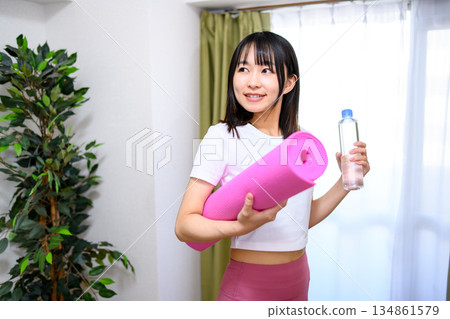 日本女子身穿瑜珈服和緊身褲,在房間裡鋪好瑜珈墊,準備了水,開始運動。 日本女子身穿瑜珈服和緊身褲,在房間裡鋪好瑜珈墊,準備了水,開始運動。 134861579