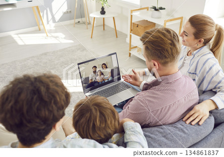 Family with children sitting on sofa using laptop and having online video call with relatives. 134861837