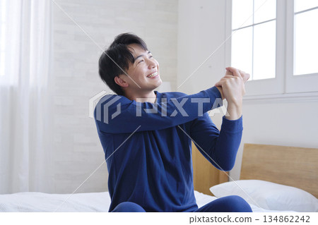 一名二十多歲的男子坐在床上伸展雙臂 134862242