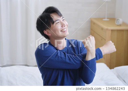一名二十多歲的男子坐在床上伸展雙臂 134862243