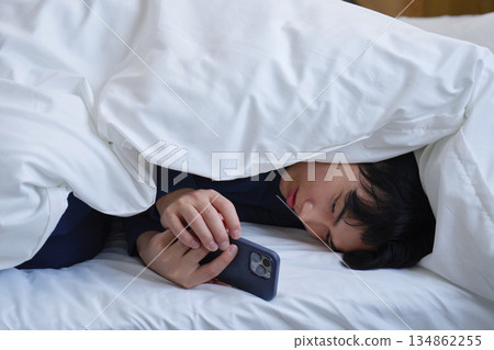 A man in his 20s using a smartphone while wrapped in a futon 134862255