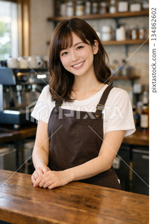 一位穿著圍裙在咖啡館工作的年輕女子。她笑容甜美。 一位穿著圍裙在咖啡館工作的年輕女子。她笑容甜美。 134862602