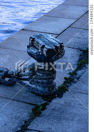 Texture of old mooring post and mooring rope standing on the quay of the port Texture of old mooring post and mooring rope standing on the quay of the port 134864191