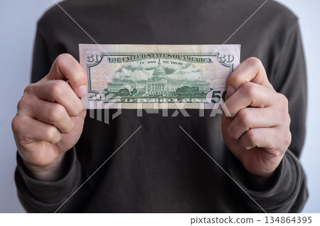 Cropped shot view of woman holding and showing fifty American dollar banknotes in hands. The US Dollar is the currency of United States. 134864395