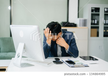 Frustrated young businessman working on a laptop computer sitting at his working place 134864995