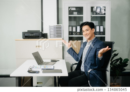 Confident businessman in suit, working on laptop and smartphone at office desk. Confident businessman in suit, working on laptop and smartphone at office desk. 134865045