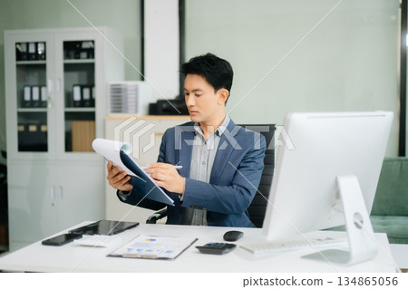 Asian businessman working with working notepad, tablet and laptop documents talking on the smartphone, tablet and laptop Asian businessman working with working notepad, tablet and laptop documents talking on the smartphone, tablet and laptop 134865056