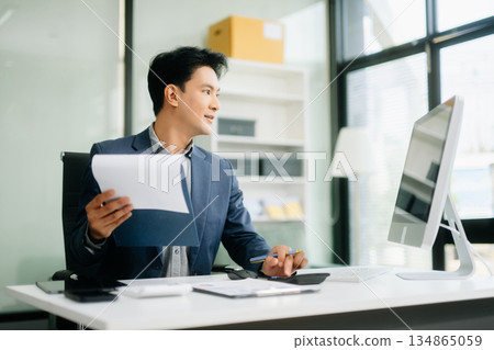 Asian businessman working with working notepad, tablet and laptop documents talking on the smartphone, tablet and laptop 134865059