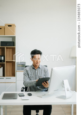 Confident business expert attractive smiling young man typing laptop and holding digital tablet on desk Confident business expert attractive smiling young man typing laptop and holding digital tablet on desk 134865073
