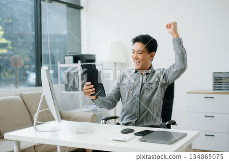 Confident business expert attractive smiling young man typing laptop and holding digital tablet on desk Confident business expert attractive smiling young man typing laptop and holding digital tablet on desk 134865075