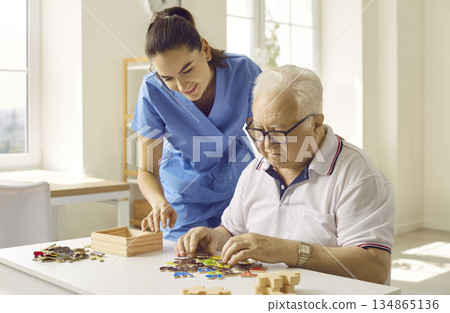 Caregiver or nurse in a retirement home helping a demented senior man with puzzles Caregiver or nurse in a retirement home helping a demented senior man with puzzles 134865136