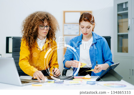 UX UI designers in modern office working on app wireframes, color palettes, and digital tools. Creative teamwork, planning, technology UX UI designers in modern office working on app wireframes, color palettes, and digital tools. Creative teamwork, planning, technology 134865333