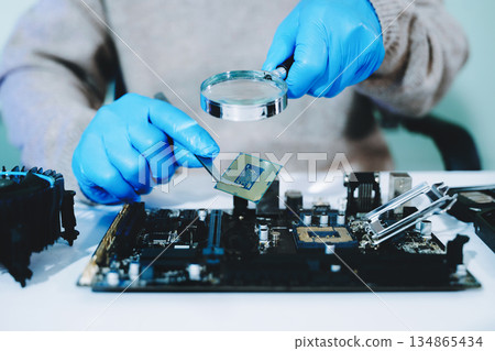 Closeup of technician inspecting CPU with magnifying glass before installing it on motherboard. Concept: repair, upgrade, precision tech work 134865434