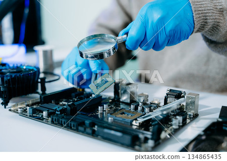 Closeup of technician inspecting CPU with magnifying glass before installing it on motherboard. Concept: repair, upgrade, precision tech work 134865435