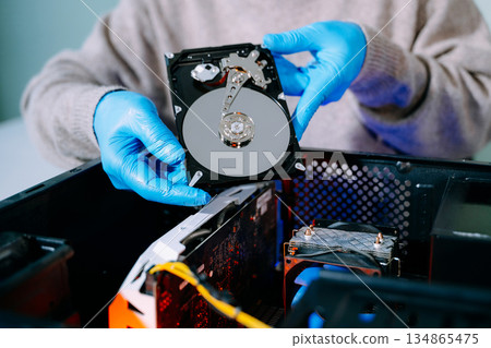 Closeup of technician with gloves holding opened hard drive above computer case, symbolizing data storage, recovery, computer repair, and IT service. Closeup of technician with gloves holding opened hard drive above computer case, symbolizing data storage, recovery, computer repair, and IT service. 134865475