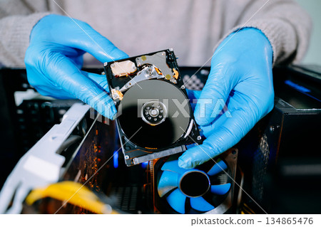 Closeup of technician with gloves holding opened hard drive above computer case, symbolizing data storage, recovery, computer repair, and IT service. Closeup of technician with gloves holding opened hard drive above computer case, symbolizing data storage, recovery, computer repair, and IT service. 134865476