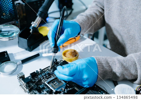 Closeup of technician soldering a computer motherboard with precision tools, showcasing electronics repair, hardware maintenance, and modern technology Closeup of technician soldering a computer motherboard with precision tools, showcasing electronics repair, hardware maintenance, and modern technology 134865498