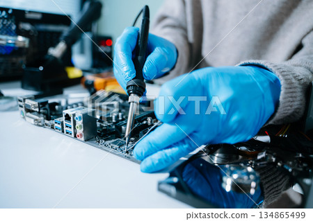 Computer technician in gloves safely repairing desktop hardware. Closeup view of hands fixing GPU and motherboard inside open PC case. Perfect for tech Computer technician in gloves safely repairing desktop hardware. Closeup view of hands fixing GPU and motherboard inside open PC case. Perfect for tech 134865499