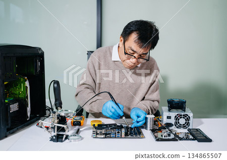 Computer technician in gloves safely repairing desktop hardware. Closeup view of hands fixing GPU and motherboard inside open PC case. Perfect for tech 134865507