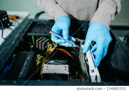 Computer technician in gloves safely repairing desktop hardware. Close-up view of hands fixing GPU and motherboard inside open PC case. Perfect for tech and repair concepts. Computer technician in gloves safely repairing desktop hardware. Close-up view of hands fixing GPU and motherboard inside open PC case. Perfect for tech and repair concepts. 134865552